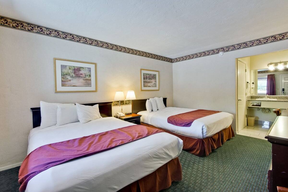 A hotel room with two beds, a vanity with a mirror, and two framed pictures on the wall.