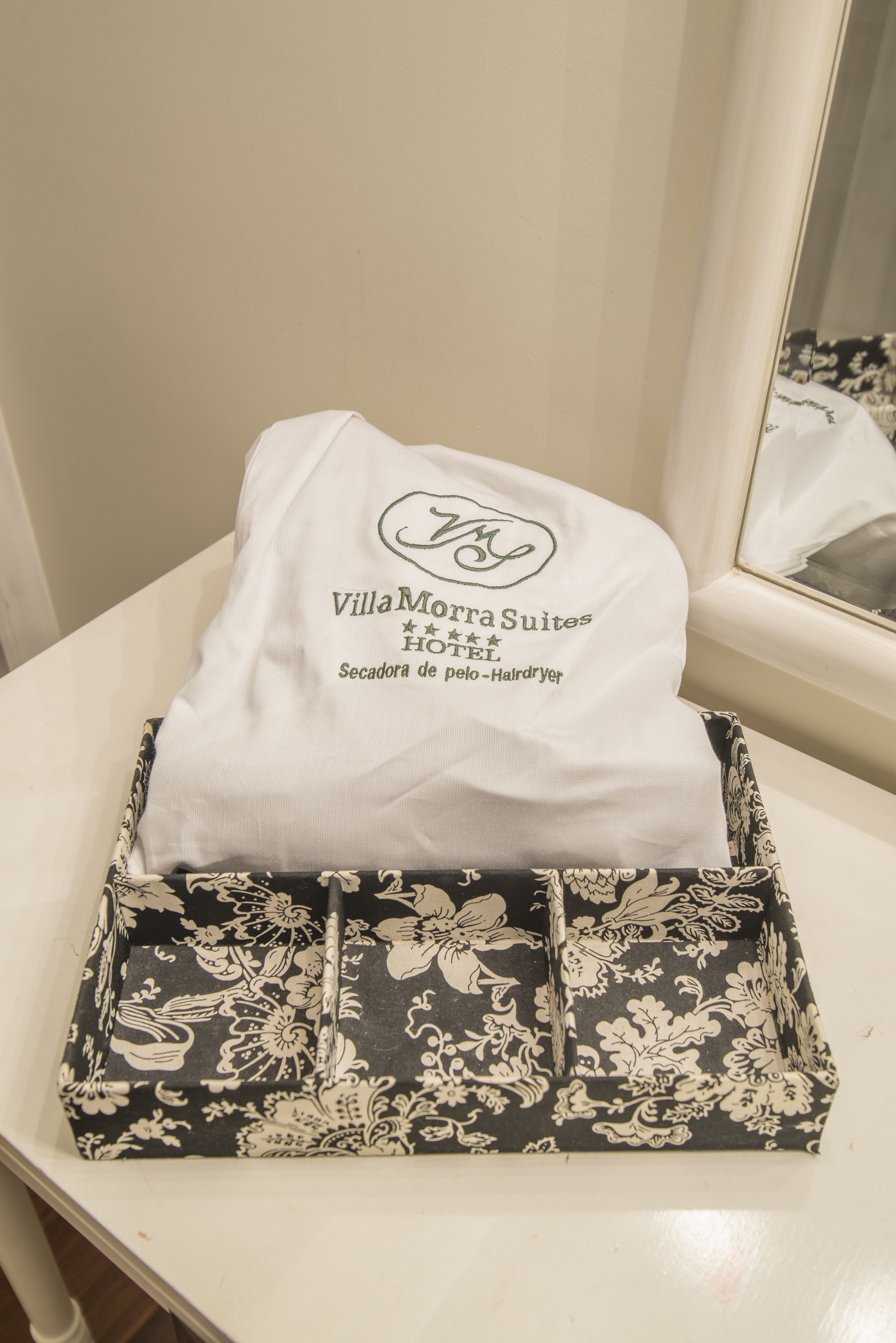 Un coussin blanc orné de motifs et de texte, ainsi qu'une boîte à motifs floraux noir et blanc, le tout posé sur une surface blanche.