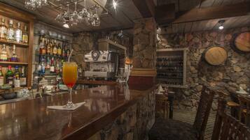 Zona de bar con mostrador de madera, una bebida en un vaso y estantes llenos de botellas de licor.