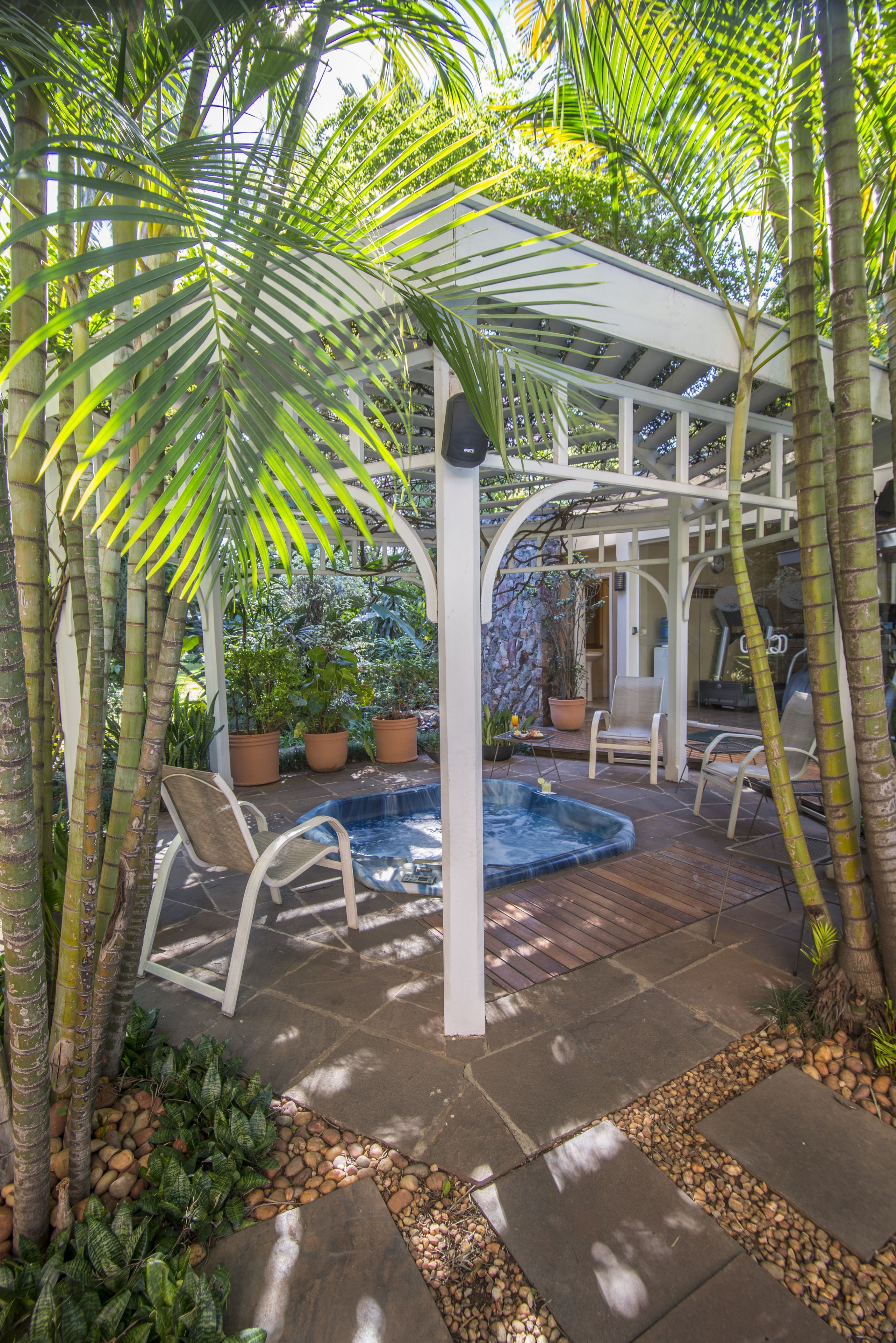 A covered outdoor area with a hot tub, seating, and potted plants.