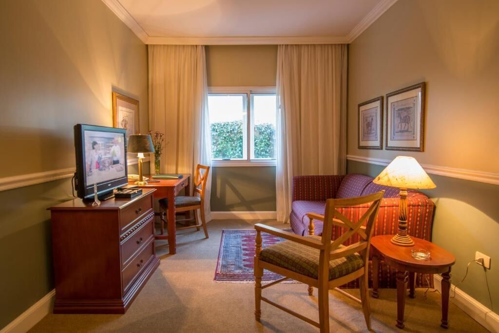 Une chambre d’hôtel de taille modeste, équipée d’une télévision, d’un bureau, d’une chaise, d’un canapé et d’une fenêtre avec des rideaux.