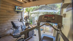 A gym with various exercise machines, a television screen, and a view of the outdoors. - Hotel Villa Morra Suites (Asunción)