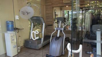Un gimnasio de hotel con equipo de ejercicio, un dispensador de agua y un reloj en la pared.