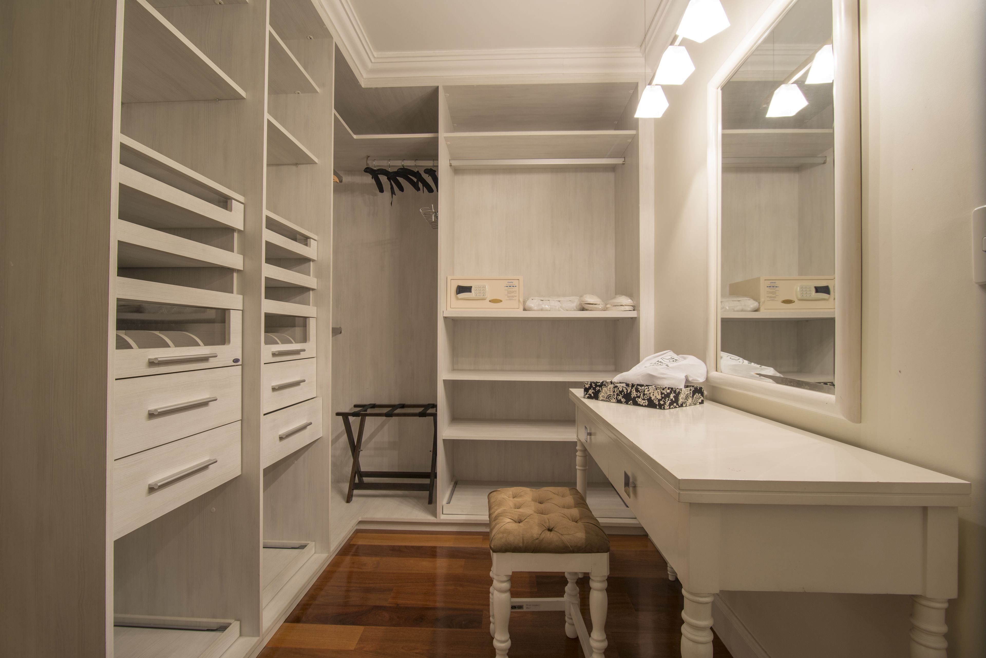 Ein begehbarer Kleiderschrank mit mehreren Regalen, Schubladen und Platz zum Aufhängen, inklusive einem Frisiertisch mit Spiegel und einer Bank.