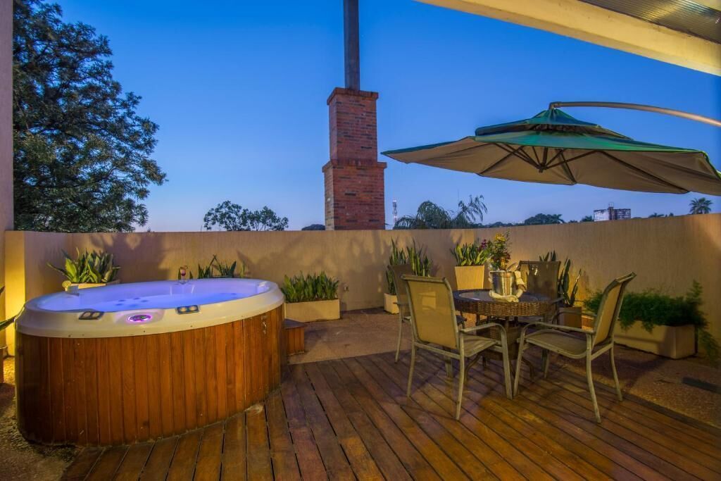 Una terraza de madera con jacuzzi, mesa exterior, sillas y sombrilla.