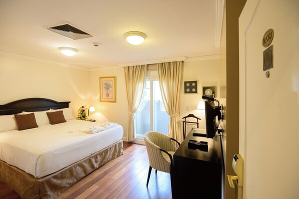 Habitación de hotel con cama, escritorio, silla y ventana con cortinas.
