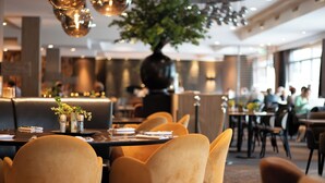 A restaurant with yellow chairs, a black vase with flowers, and a large tree in the center.
