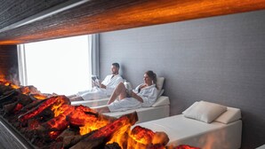 A room with a fireplace, two white beds, and a large window.