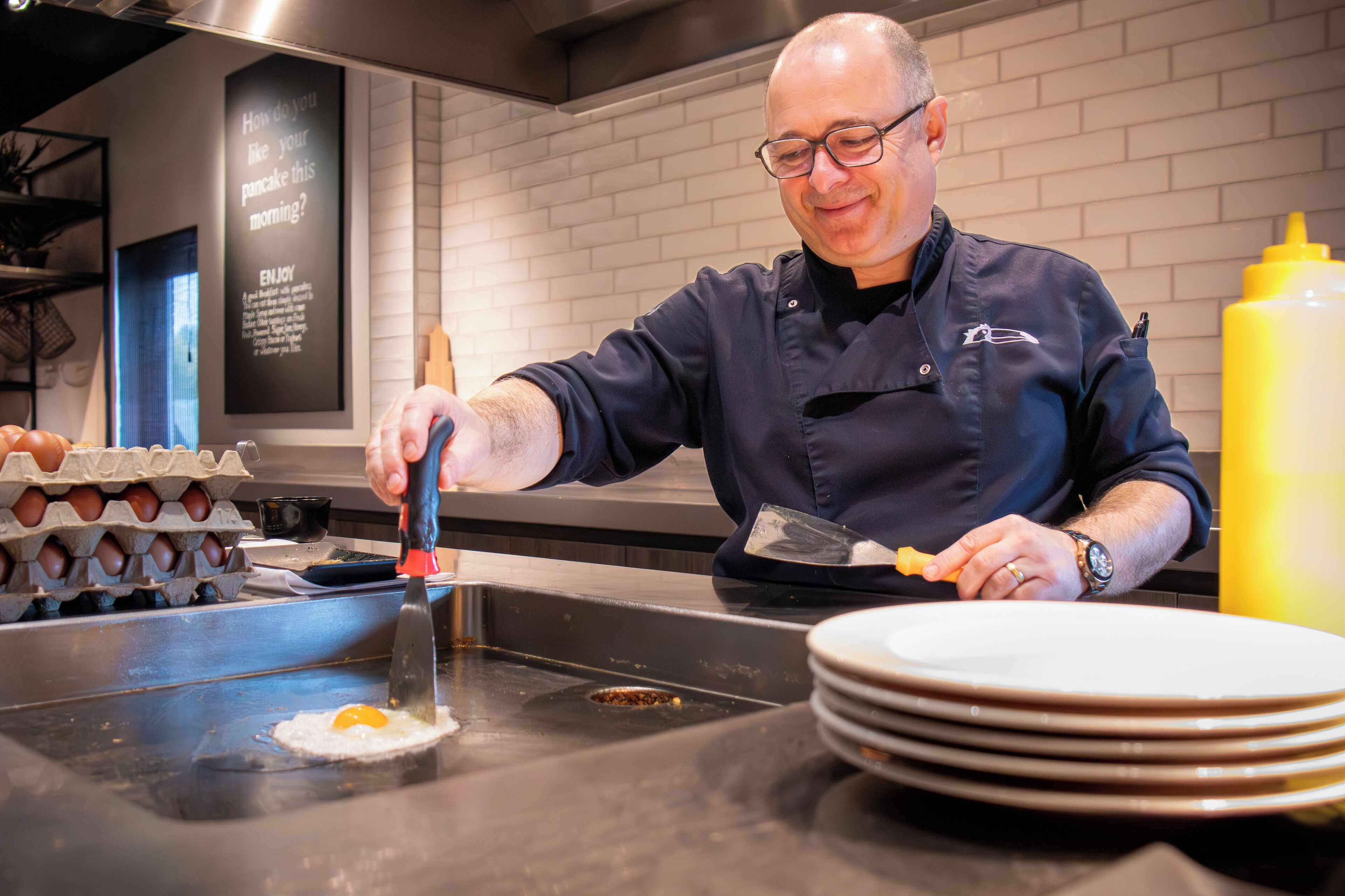 Een kok bereidt eten aan een toonbank, met eieren, een koekenpan en een stapel borden.