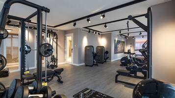 Ein Fitnessraum mit verschiedenen Trainingsgeräten, einer Hantelbank und einer Trainingsmatte mit Übungsanleitungen.