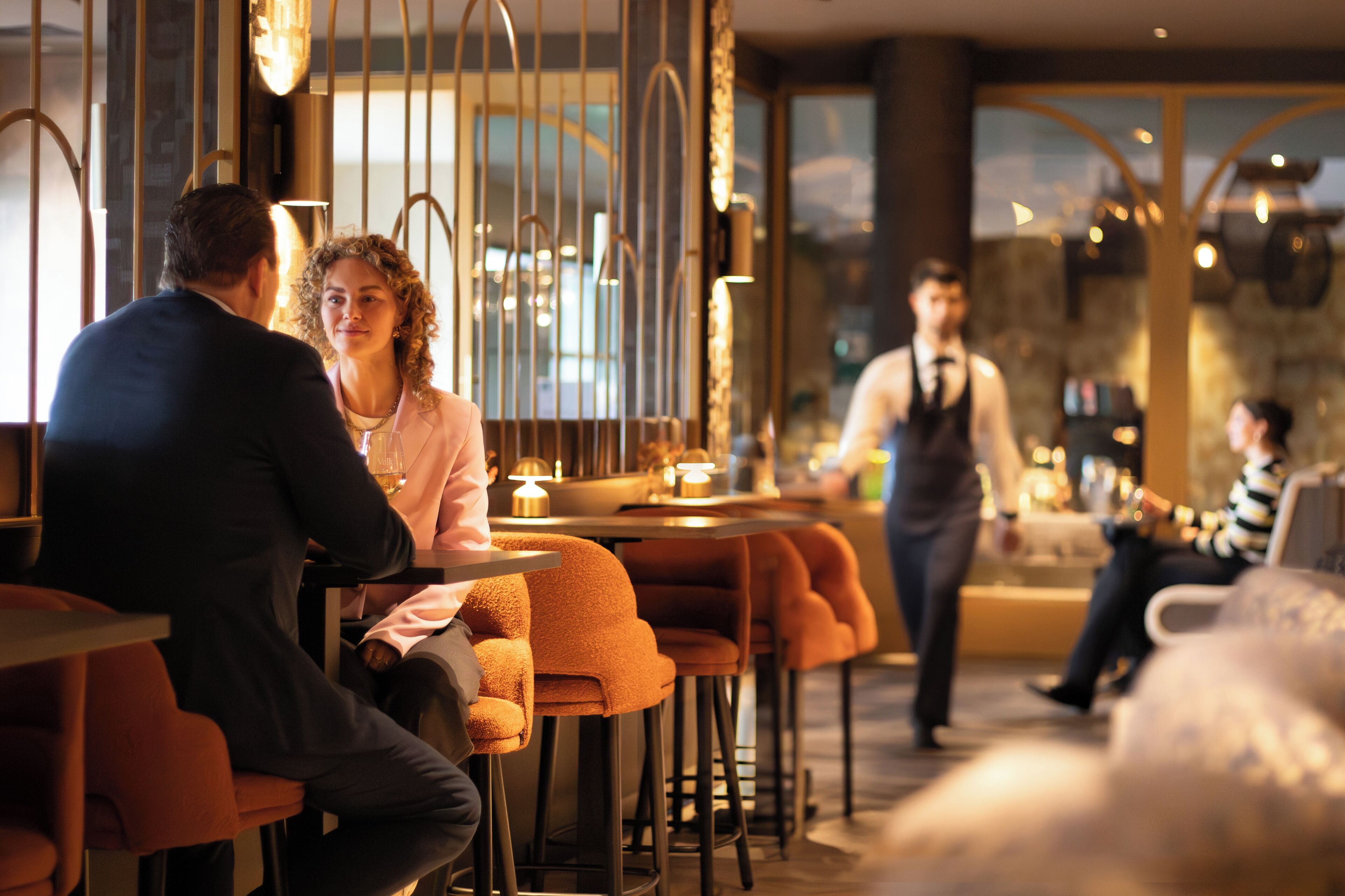 Interior moderno de un restaurante con barra, asientos y un camarero atendiendo a los clientes.