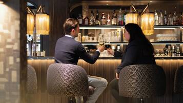 A bar area with two stools, a bar counter with various bottles, and hanging lamps.