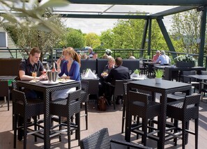 Un área de comedor al aire libre con mesas y sillas de mimbre, rodeada de follaje y una sección cubierta.