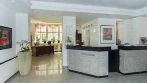 Een hotel receptie met een gepolijst granieten aanrecht, een receptiebalie en een groot raam met gordijnen.
