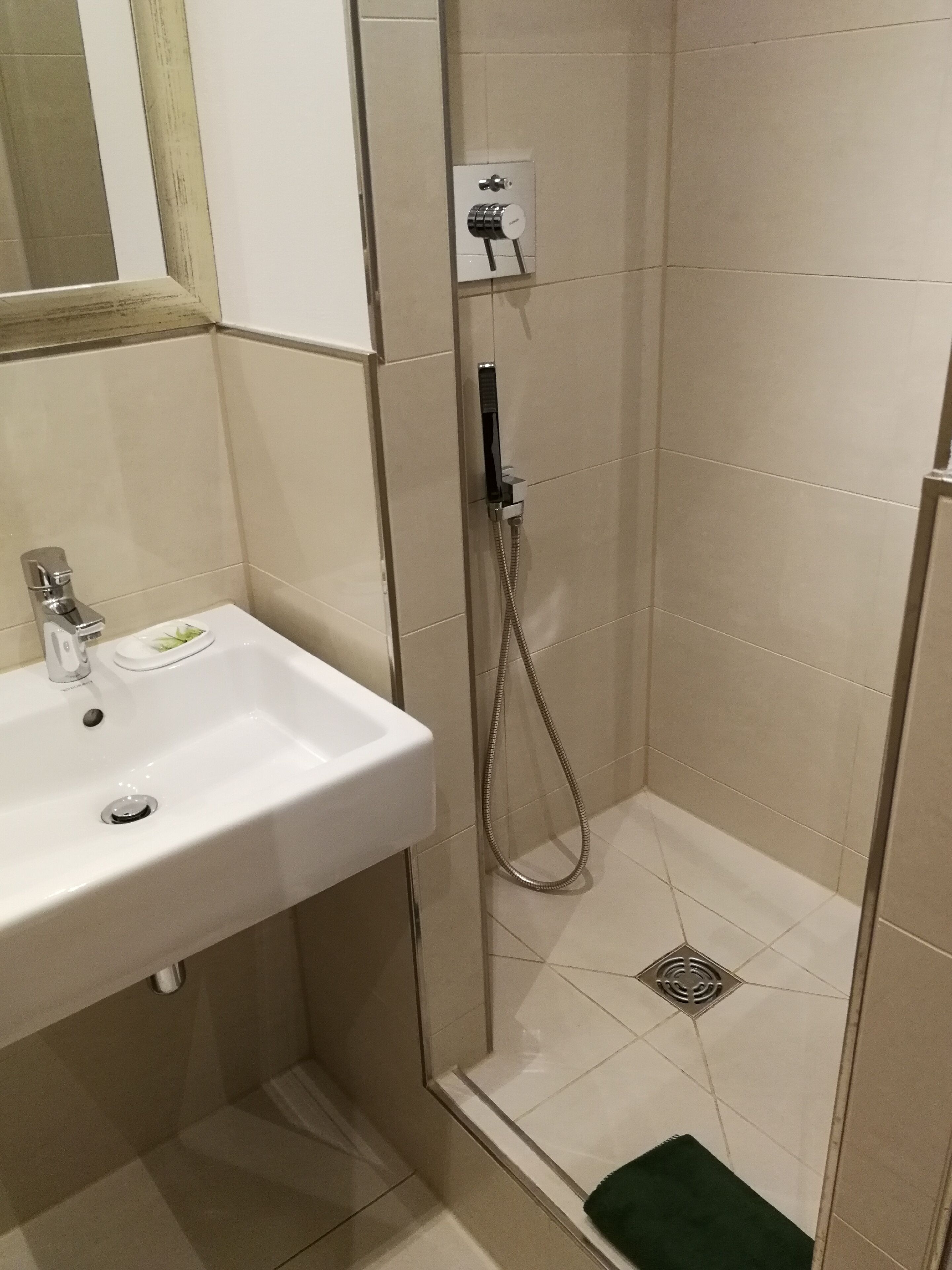 A bathroom with a white sink, a shower with a handheld showerhead, and a green bath mat.