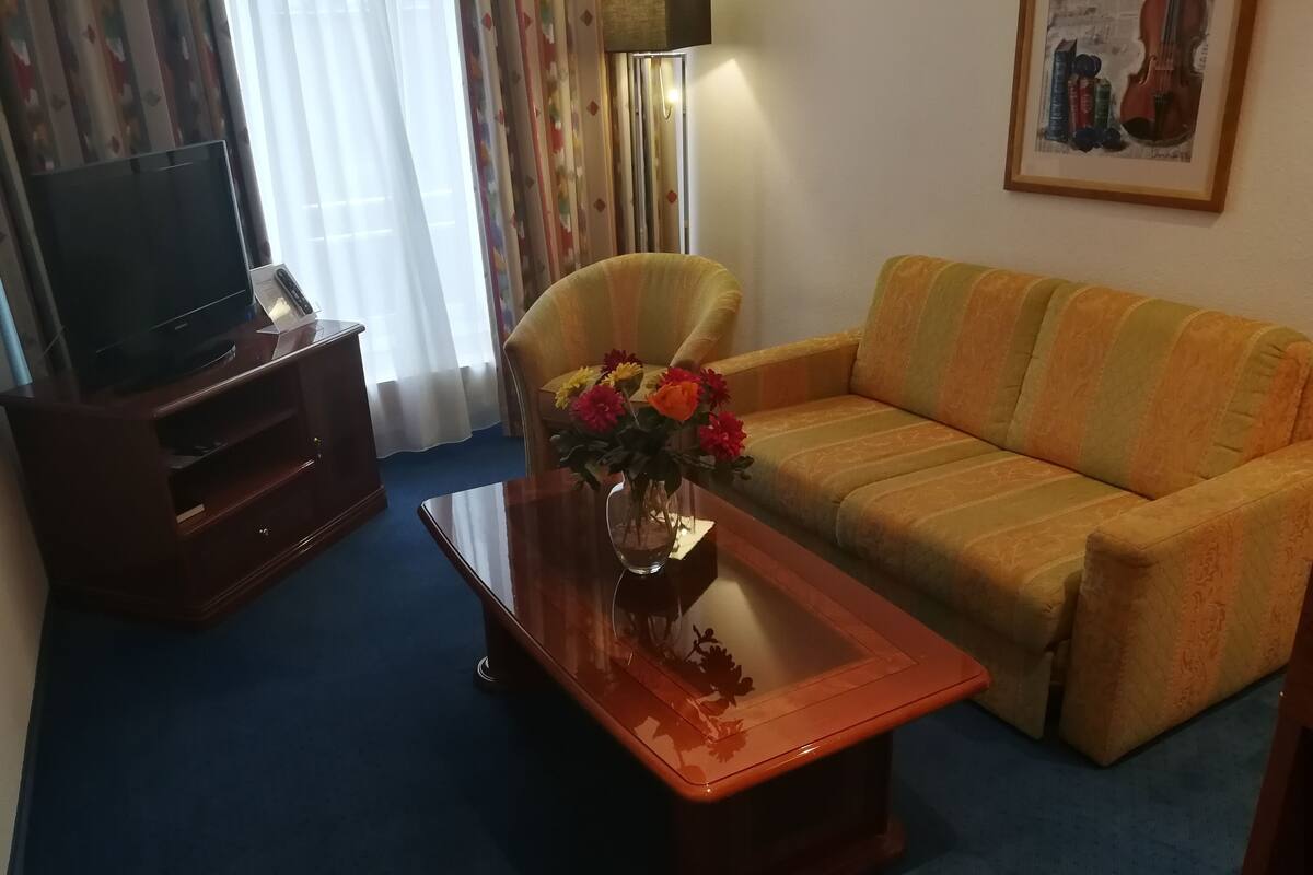 A living room with a sofa, a coffee table with a vase of flowers, a TV on a stand, and a lamp.