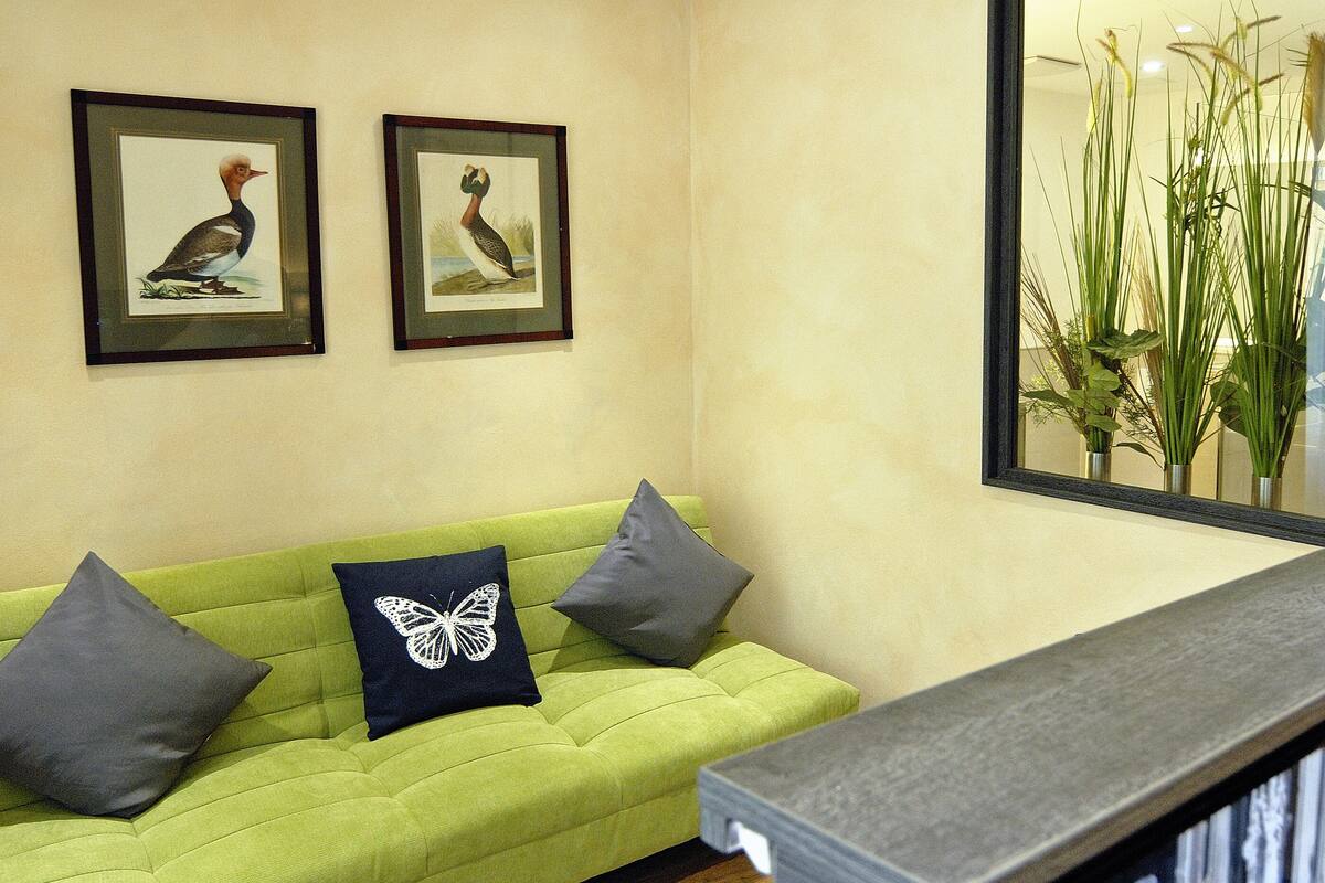 A living room with a green sofa, two framed pictures on the wall, a flat-screen TV, and a telephone on the floor.