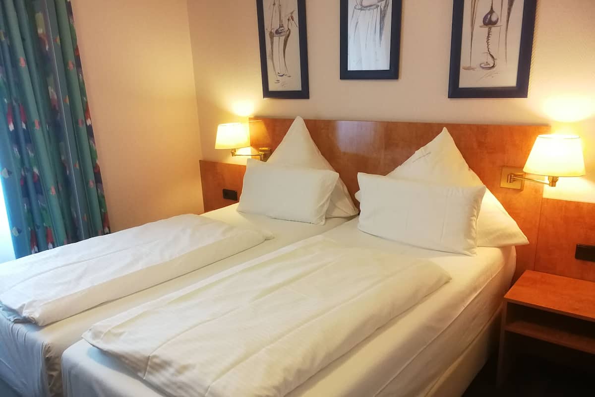 A double bed with white linens, two bedside tables with lamps, and three framed artworks on the wall.