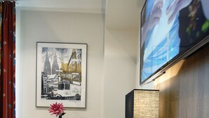 Een hotelkamer met een houten bureau, een laptop, een telefoon, een lijst in een fotokader aan de muur en een televisie boven het bureau.