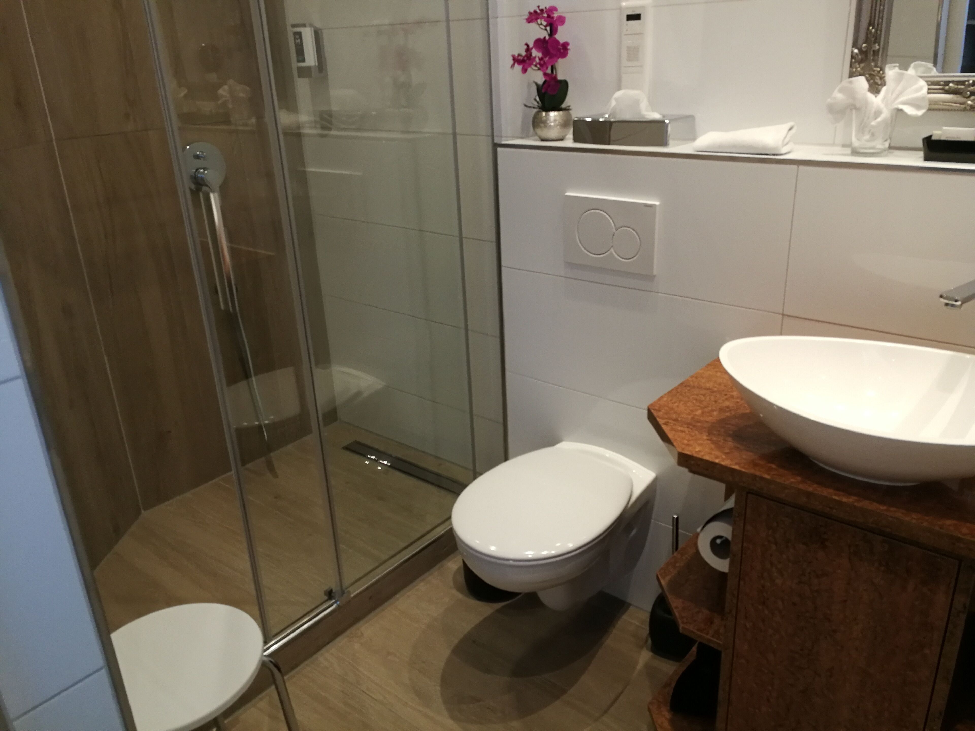 Un bagno moderno con cabina doccia in vetro, un water bianco e un lavabo a vasca su un piano in legno.