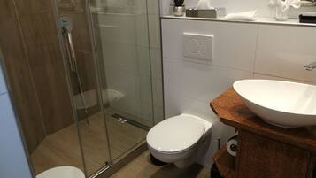 Un bagno moderno con cabina doccia in vetro, un water bianco e un lavabo a vasca su un piano in legno.