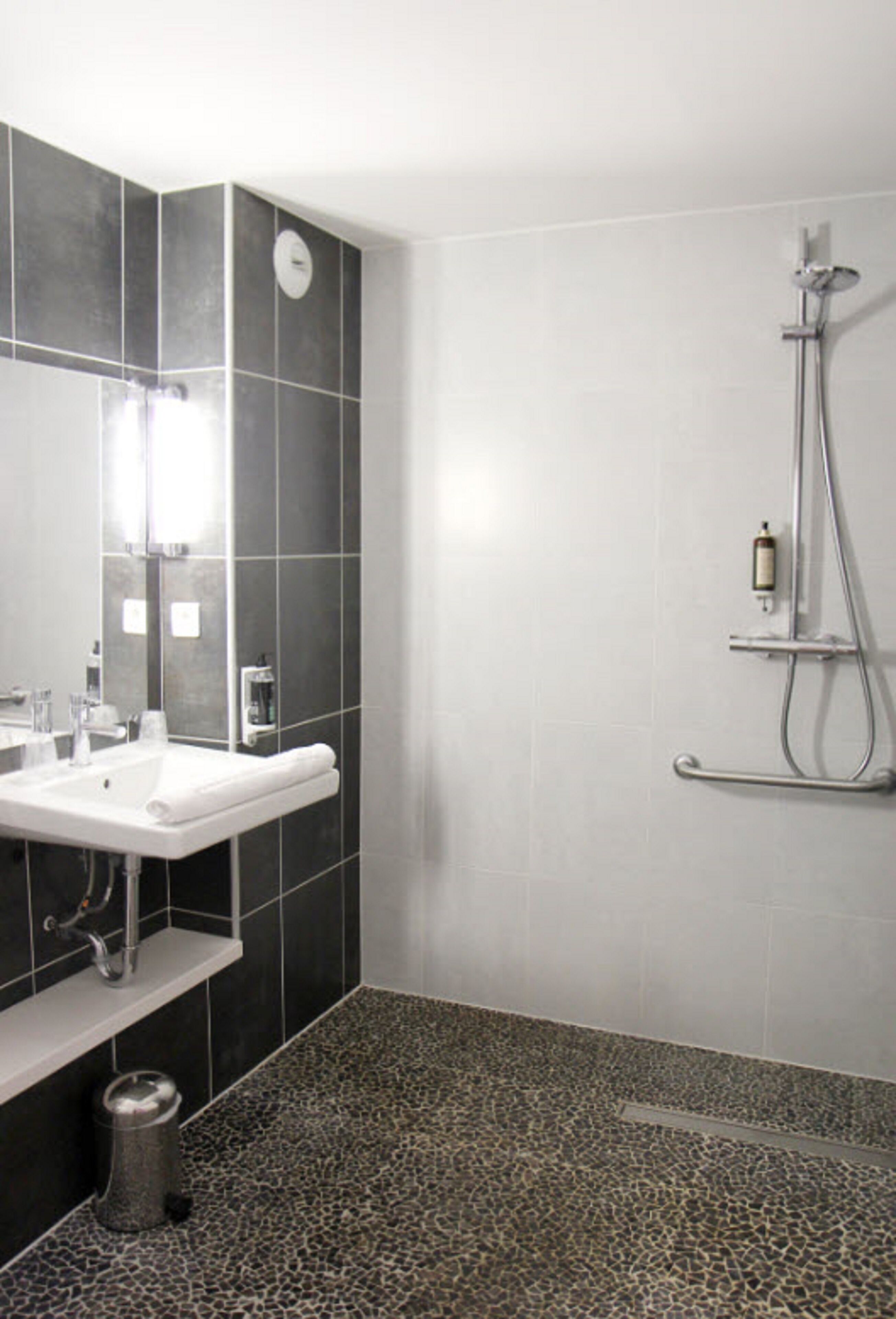 A modern bathroom with a white sink, dark tiled walls, and a shower area.