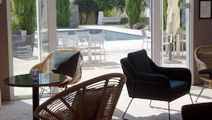 Un espacio interior moderno con un ventanal que da a una zona de piscina, amueblado con sillas de mimbre y una mesa de vidrio.