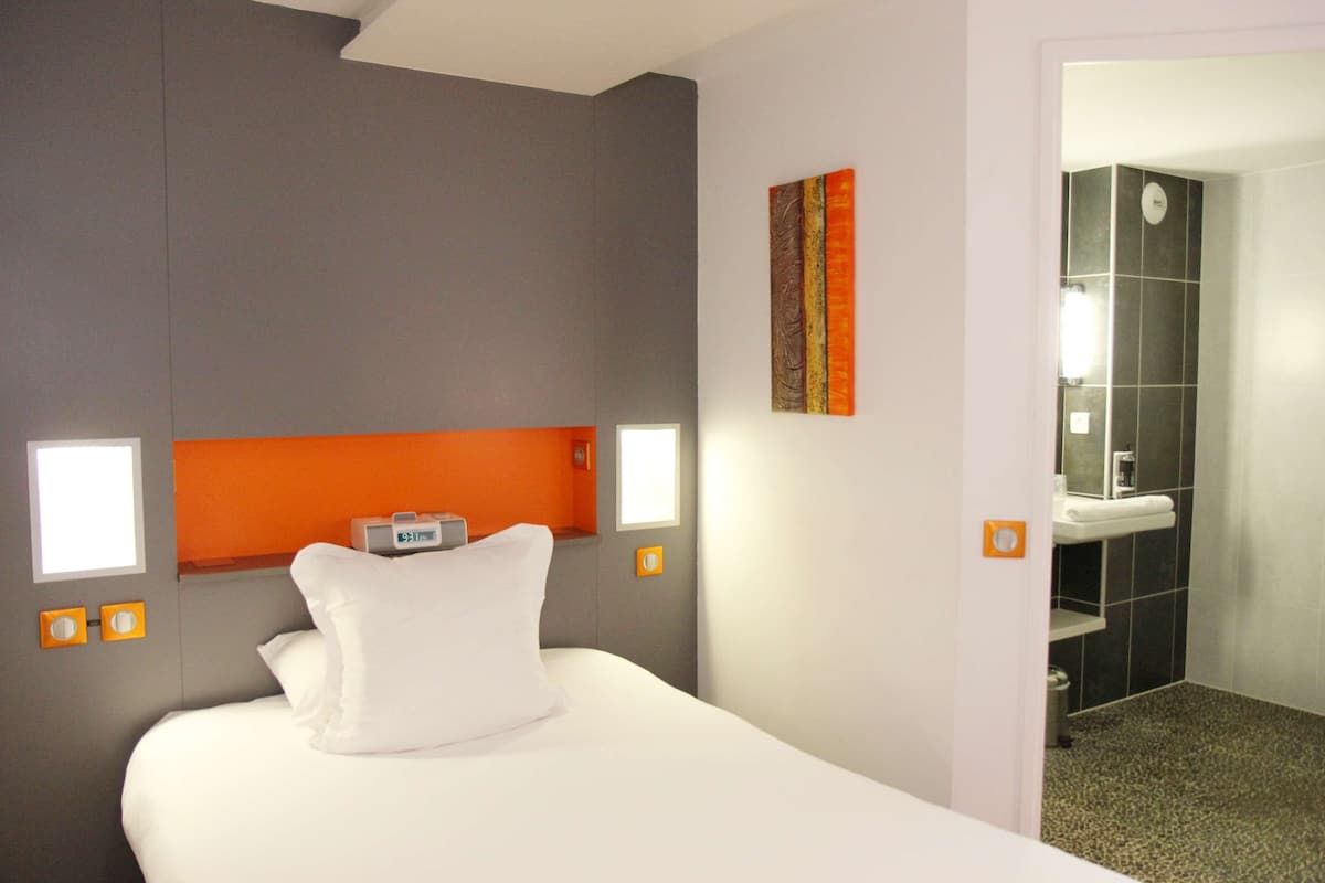 Ein Hotelzimmer mit einem Bett, einem Kopfteil, einer an der Wand montierten Uhr, einem Gemälde und einem durchgegangenen Tür sichtbaren Badezimmer.