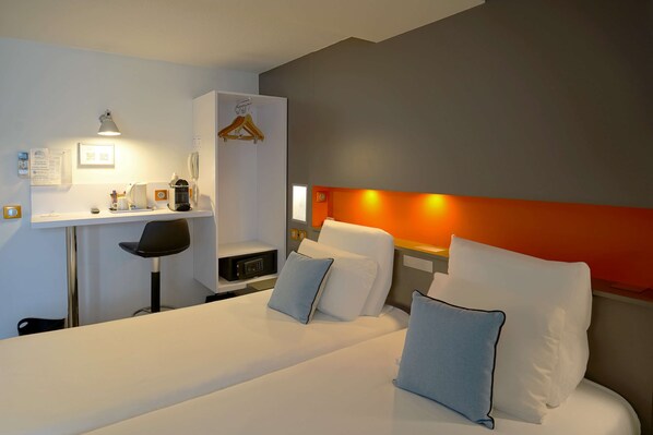 Una habitación de hotel con cama, mesita de noche, silla, escritorio y un pequeño estante.