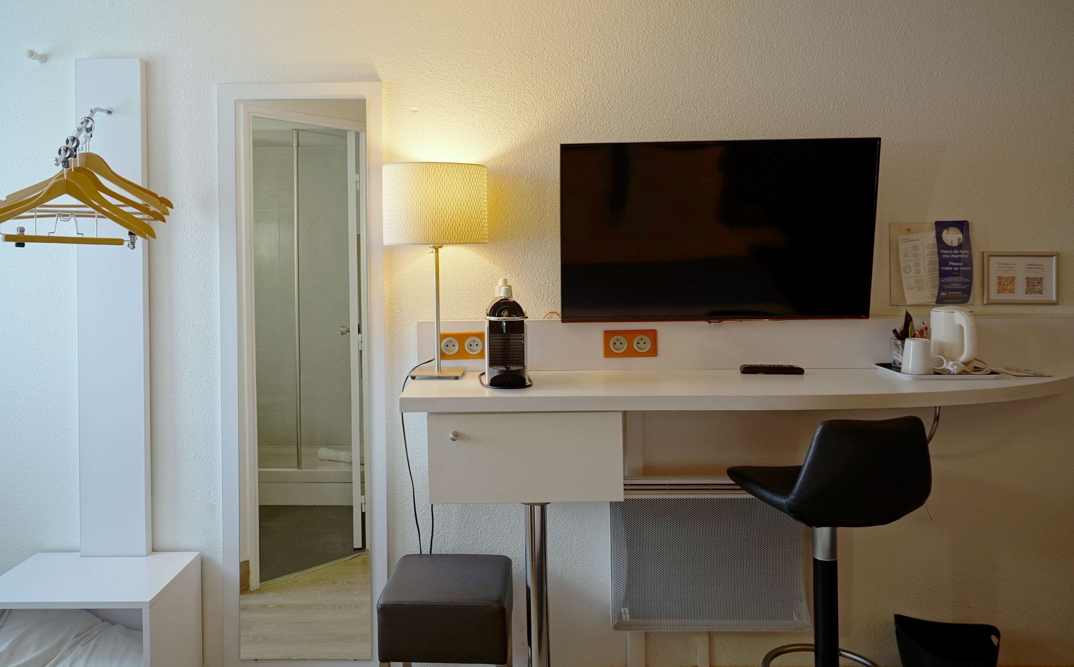 Una habitación de hotel moderna con un escritorio, televisor, lámpara y una silla.