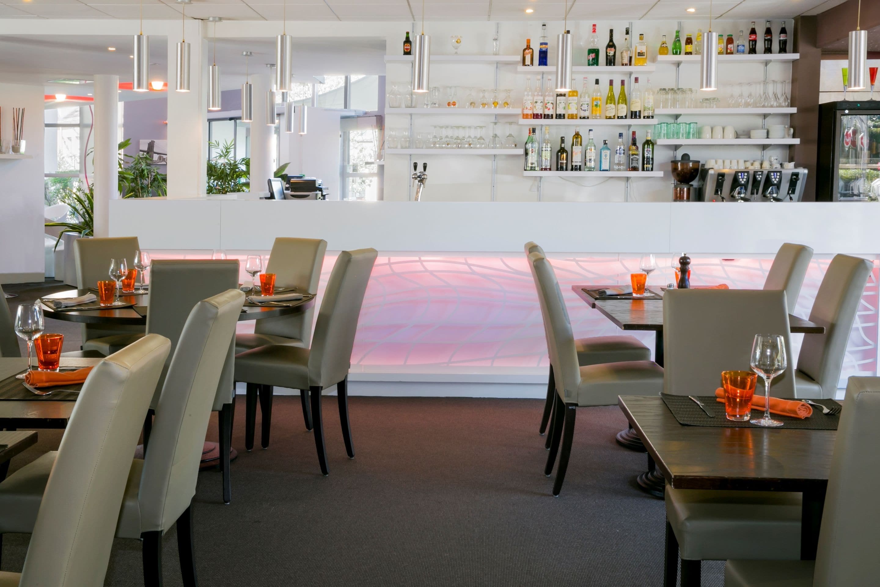 Un restaurant doté d’un bar, de tables avec des chaises et offrant une vue à travers une paroi vitrée.
