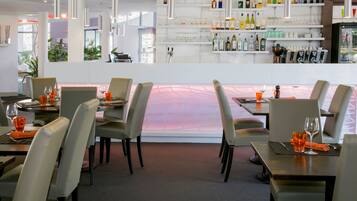 Un restaurant doté d’un bar, de tables avec des chaises et offrant une vue à travers une paroi vitrée.