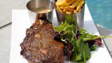 Un plato con bistec, papas fritas y ensalada junto a una piscina.