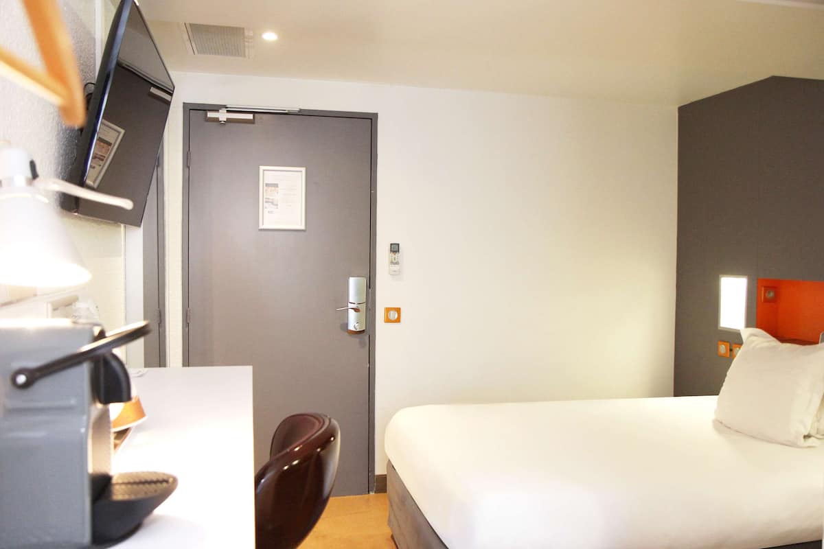 Ein Hotelzimmer mit einem Bett, einem Schreibtisch mit Lampe, einem Sessel und einer Tür mit Schild.