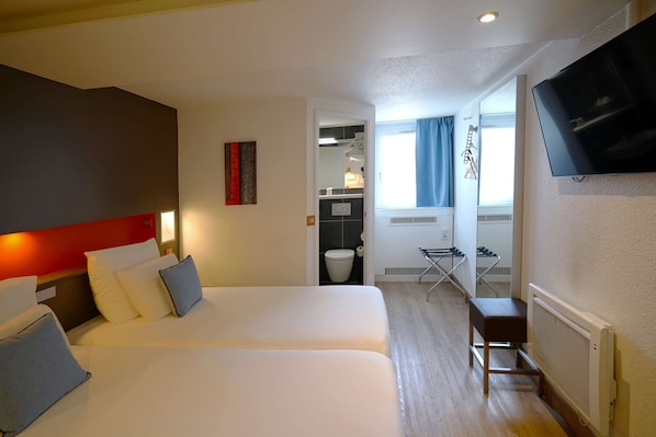 Habitación de hotel con dos camas, televisión, baño con espejo y ventana con cortinas.