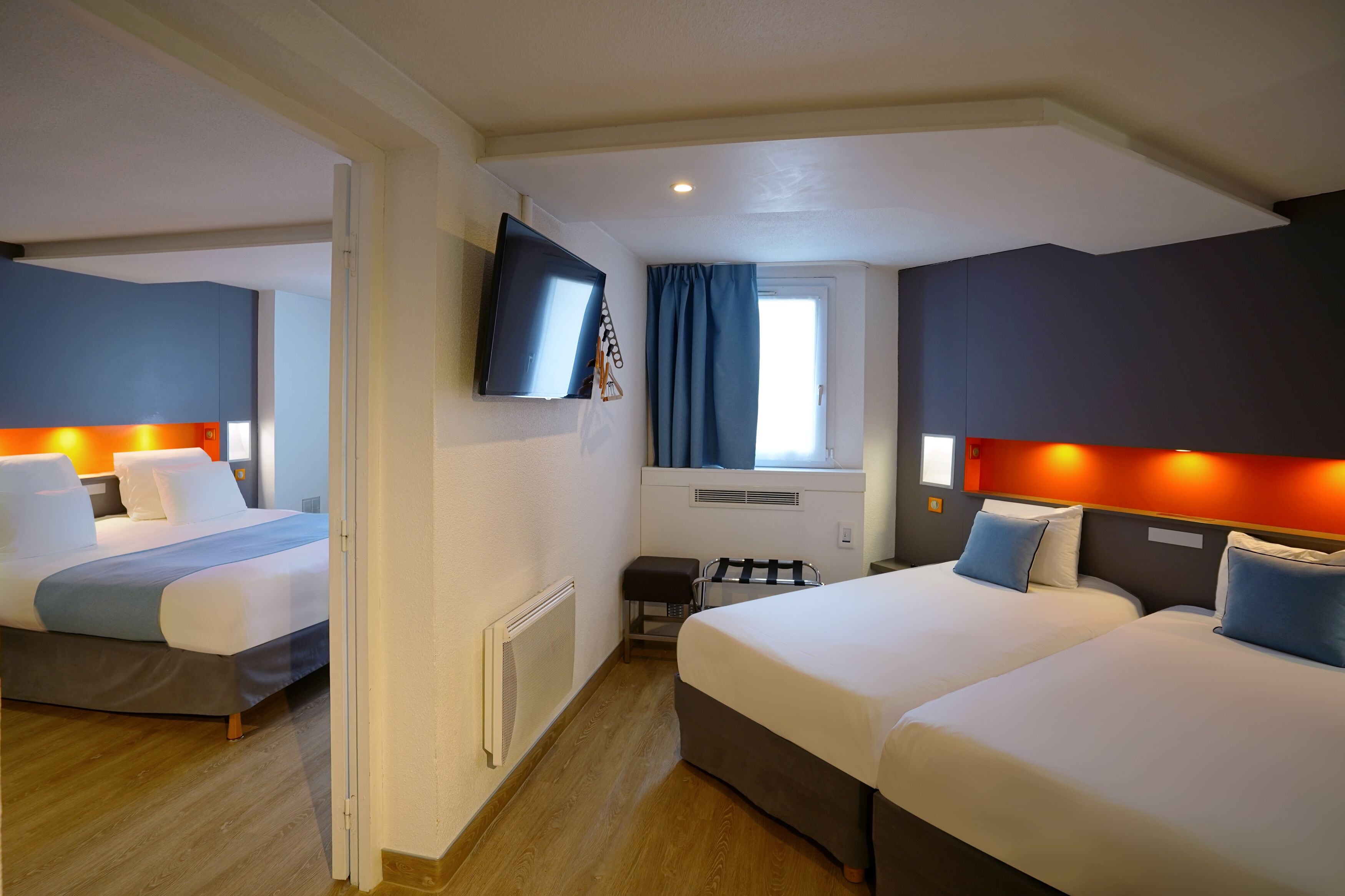A hotel room with two beds, a TV mounted on the wall, and a window with curtains.