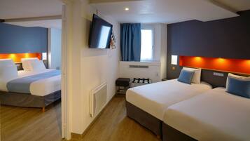 Ett hotellrum med två sängar, en tv som är monterad på väggen och ett fönster med gardiner.