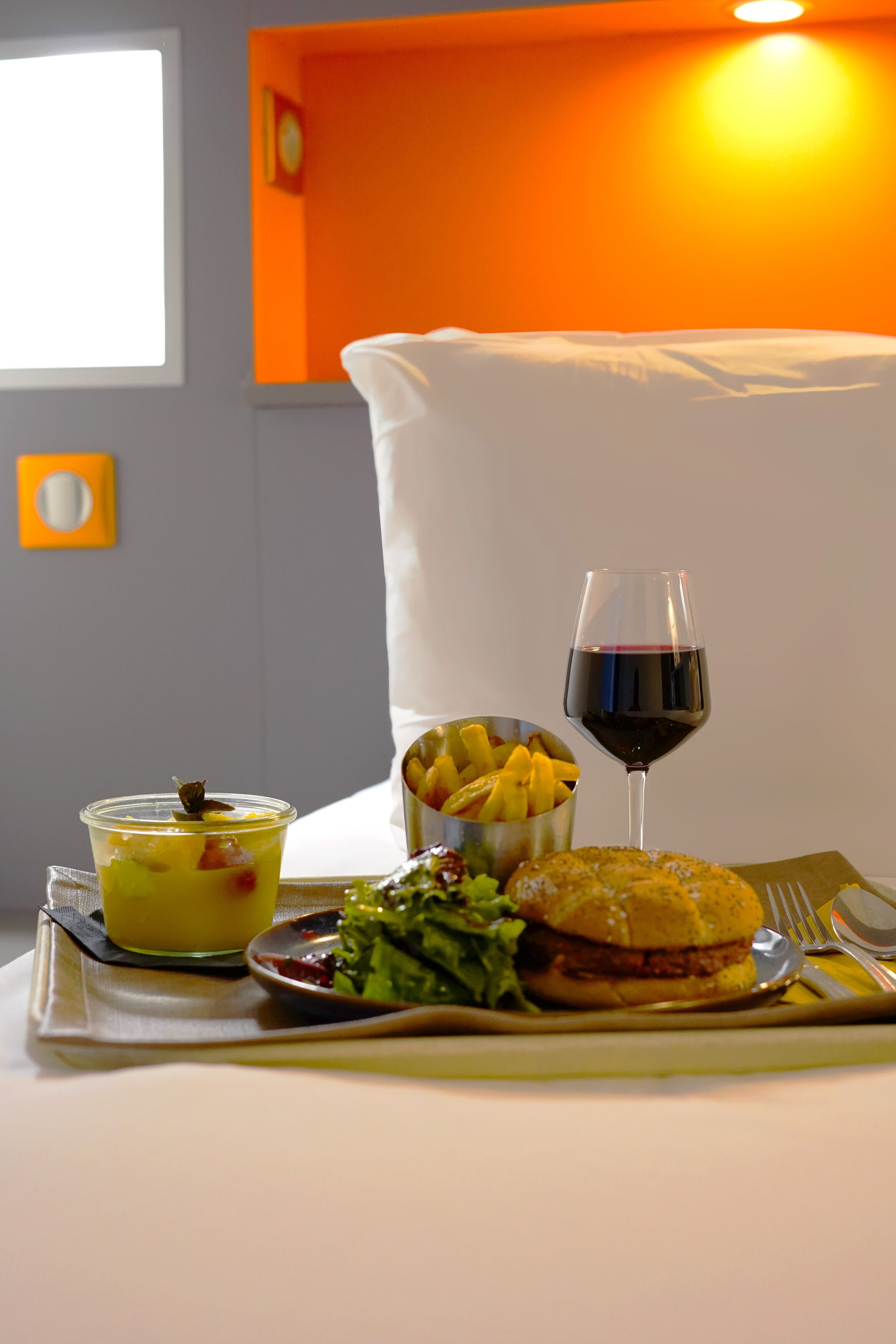 Una mesa lista para comer, con comida, una copa de vino tinto y una cama al fondo.