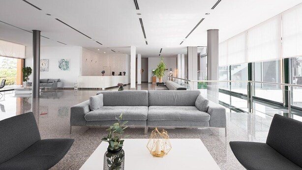 A modern lobby with a grey sofa, two armchairs, a white coffee table, and a hanging plant. - Exe Via Argentum (Silleda)