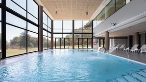 An indoor swimming pool with clear glass walls, a view of the outdoors, and lounge chairs along the side. - Exe Via Argentum (Silleda)