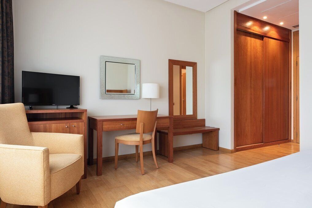 Una habitación de hotel con cama, escritorio, silla, televisión, espejo y armario.