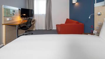 Hotelkamer met een bed, een bureau met een computer, een stoel, een televisie en een rode fauteuil.
