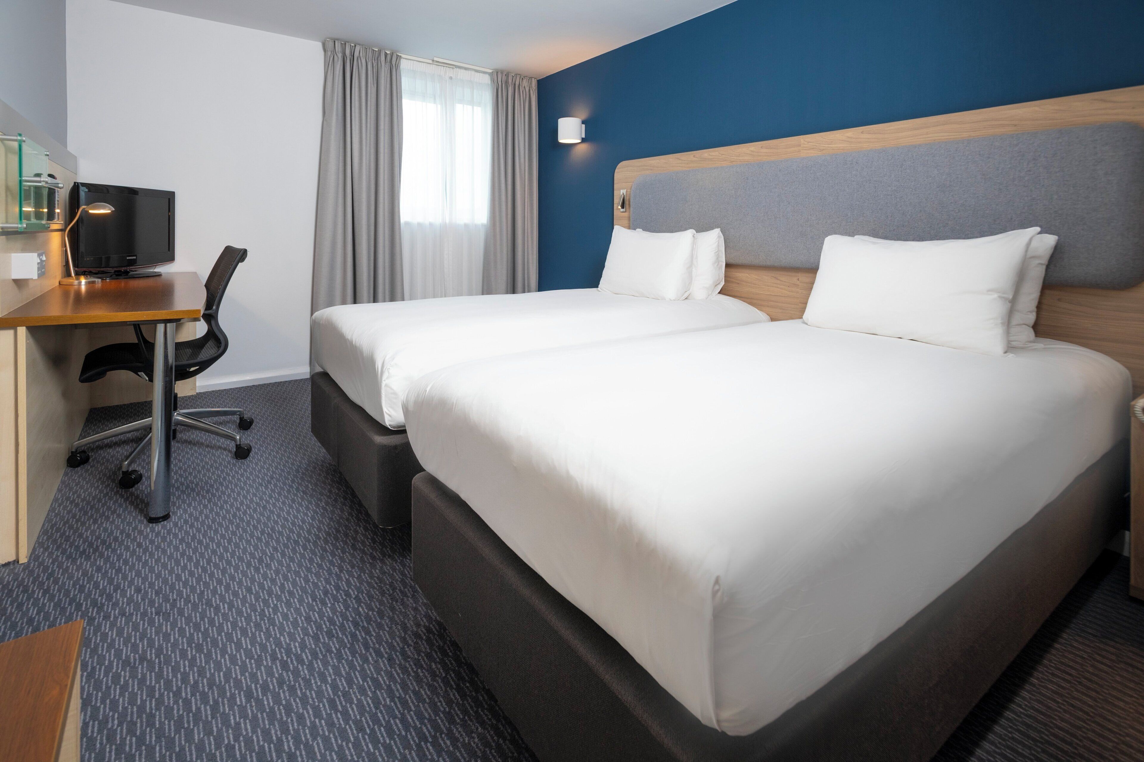 A hotel room with two beds, a desk with a computer, and a chair.