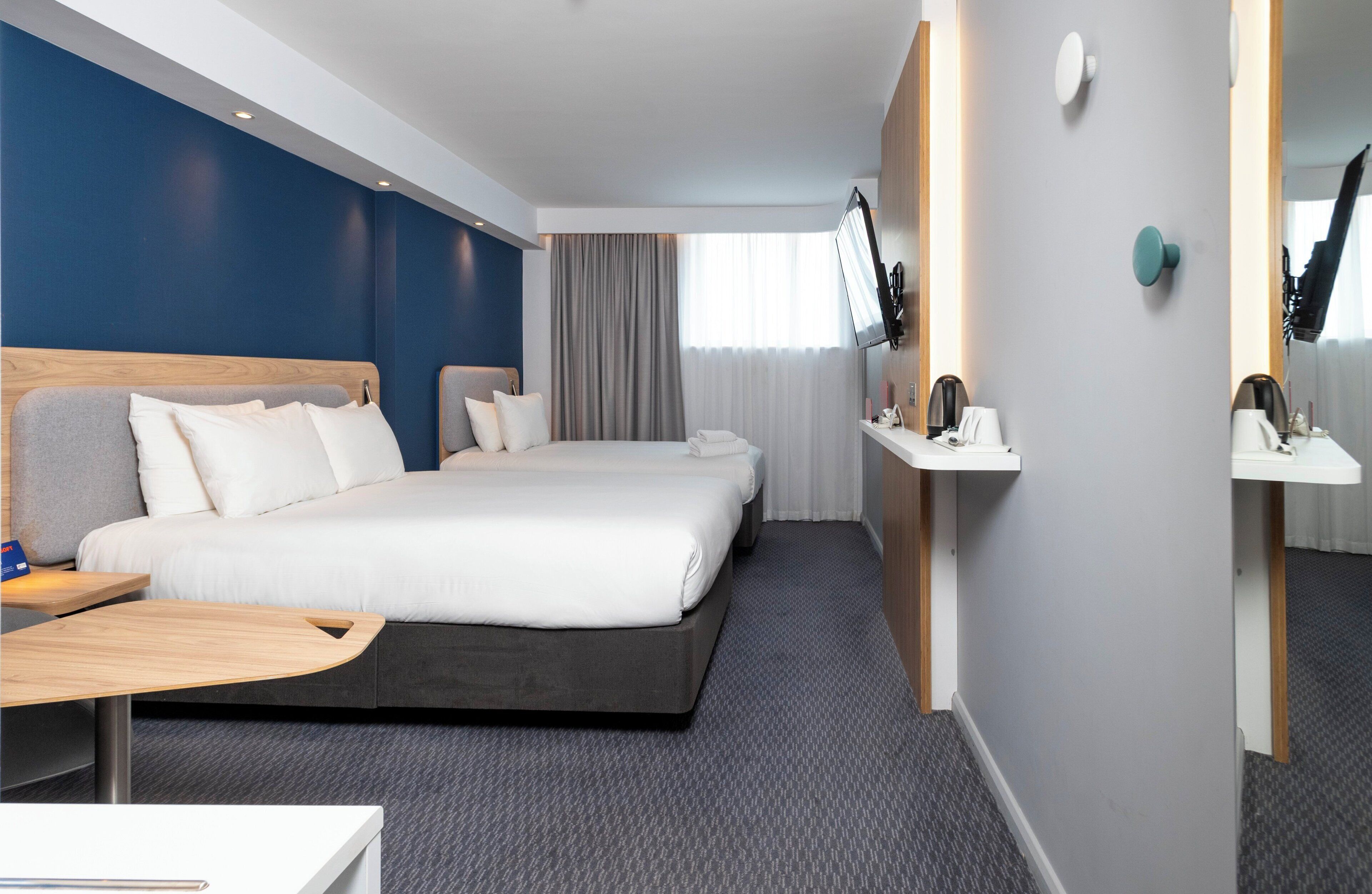 A hotel room with a large bed, a desk, a TV, and a mirror.