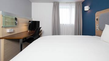 Habitación de hotel con una cama grande, un escritorio con ordenador, un espejo y una ventana con cortinas.