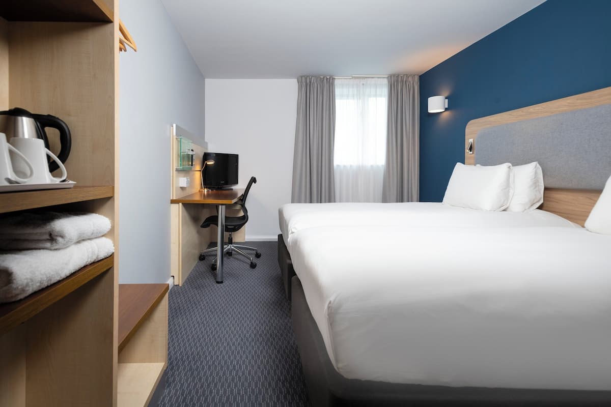 A hotel room with a large bed, a desk with a chair, a television, and a shelf with towels.