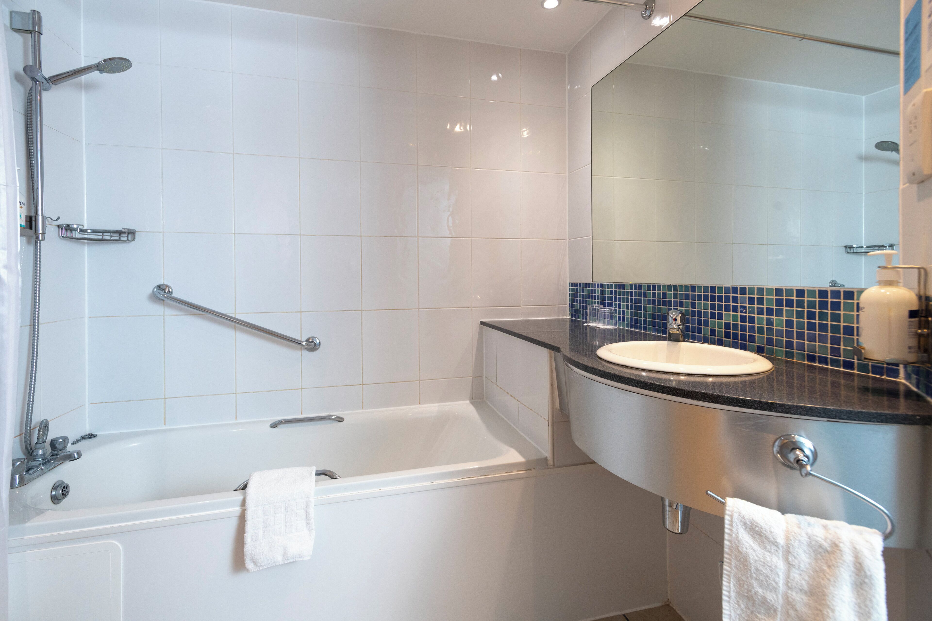 Une salle de bain moderne avec une baignoire blanche, un lavabo avec un pare-éclaboussures bleu et un grand miroir.