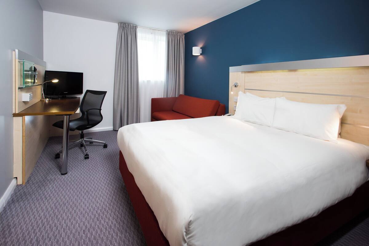 A hotel room with a large bed, a desk with a computer, a chair, and a TV.