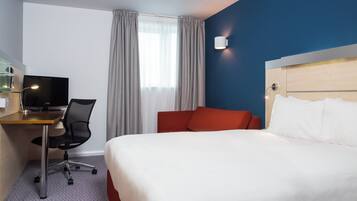 Habitación de hotel con cama, escritorio con ordenador, silla, televisor y ventana con cortinas.