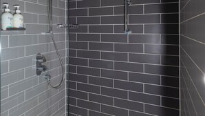 Un baño moderno con cabina de ducha de vidrio, paredes cubiertas de azulejos oscuros y una bañera blanca.